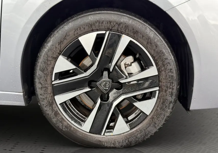 Gros plan sur la roue avant droite d’une Peugeot 208 gris clair, jante alliage bicolore moderne.
