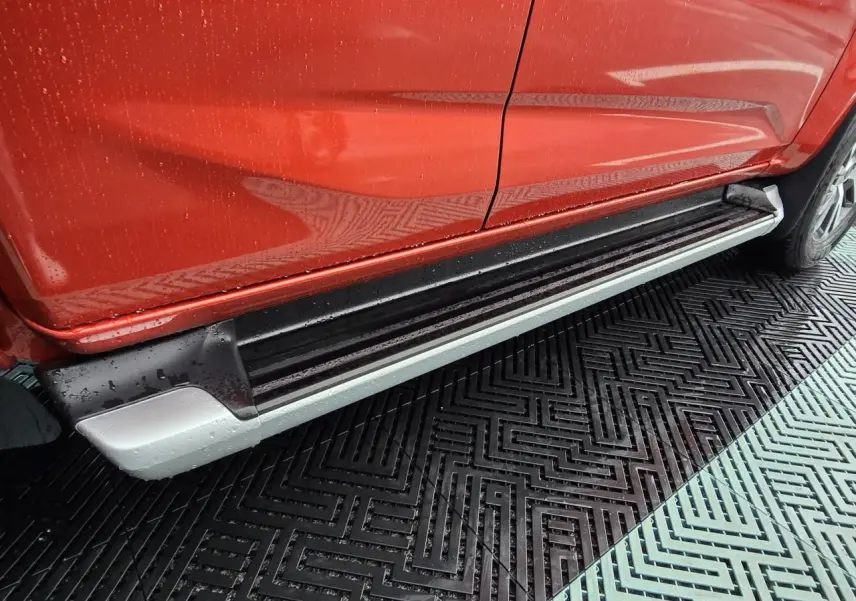 Vue latérale droite du pick-up Isuzu D-MAX orange métallisé, mettant en valeur le marchepied argenté et noir sous la porte.