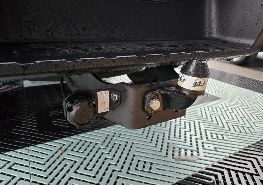 Gros plan sur l'attelage noir sous la benne d'un Isuzu D-MAX orange métallisé, avec bouchon de protection marqué gdlw.