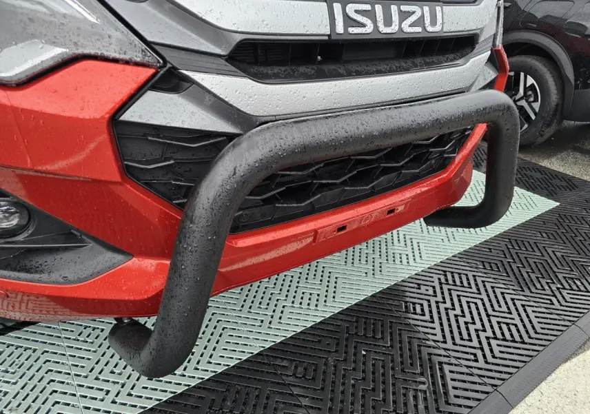 Gros plan sur la face avant orange métallisée d'un Isuzu D-MAX avec bullbar noir et calandre chromée sous la pluie.