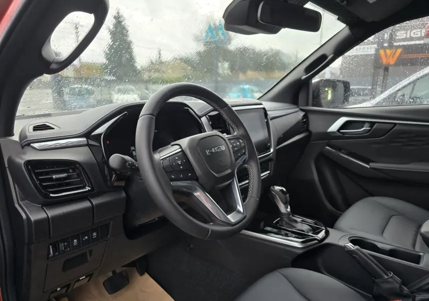 Intérieur de l'Isuzu D-MAX 2025 vu côté conducteur, volant cuir et console centrale avec levier de boîte auto.