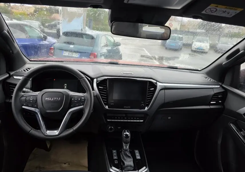 Intérieur noir du pick-up Isuzu D-MAX 2025 vu de face, avec volant cuir et écran tactile central éteint.