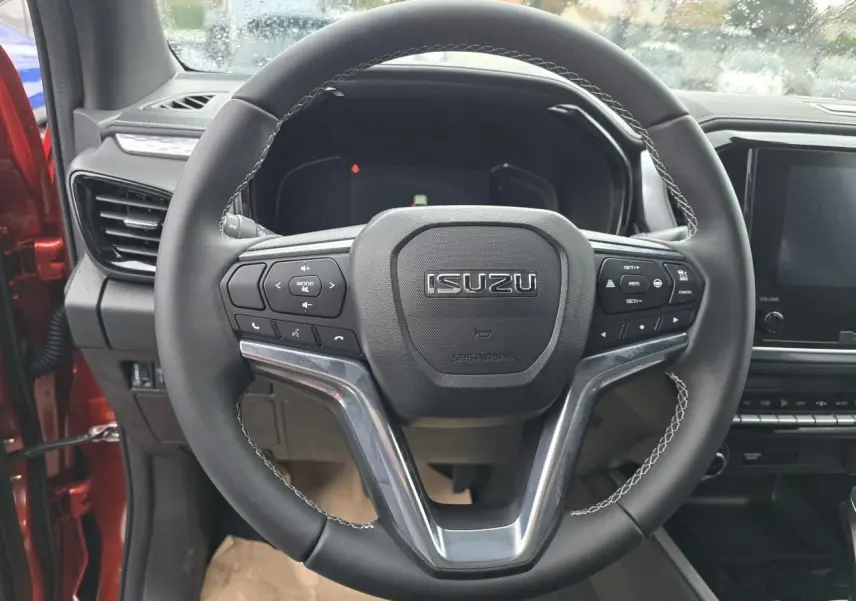 Volant en cuir avec commandes multifonctions de l'Isuzu D-MAX 2025, intérieur côté conducteur visible en orange métallisé.