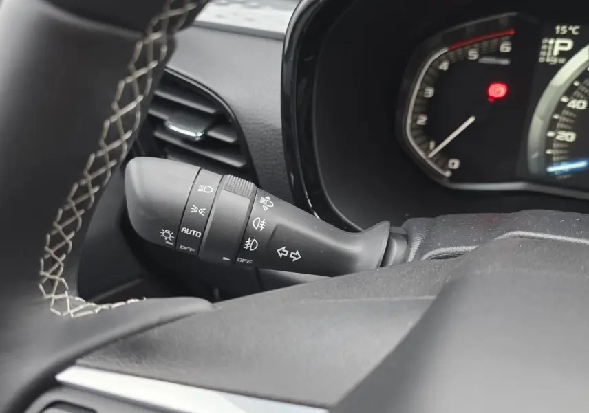 Gros plan sur la commande des phares et clignotants noire, tableau de bord et volant en cuir gris d'un Isuzu D-MAX orange métallisé.