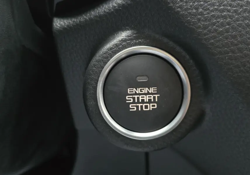 Gros plan sur le bouton noir de démarrage moteur cerclé de chrome dans l'habitacle du pick-up Isuzu D-MAX orange métallisé.