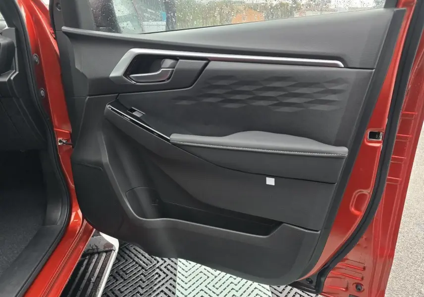 Porte côté gauche ouverte d'un Isuzu D-MAX orange métallisé, intérieur noir avec poignée et accoudoir design.