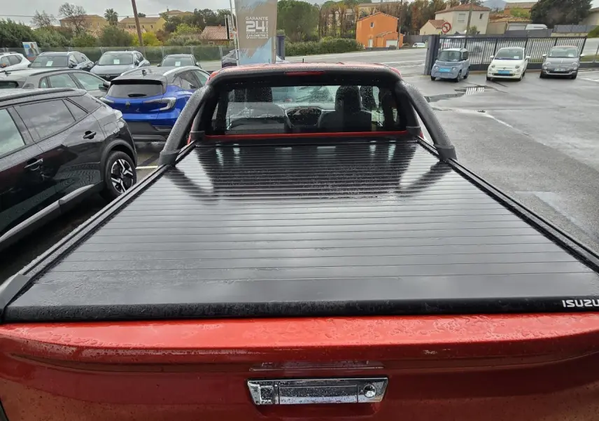 Vue arrière d'un pick-up Isuzu D-MAX orange métallisé avec benne couverte par un rideau rigide noir.