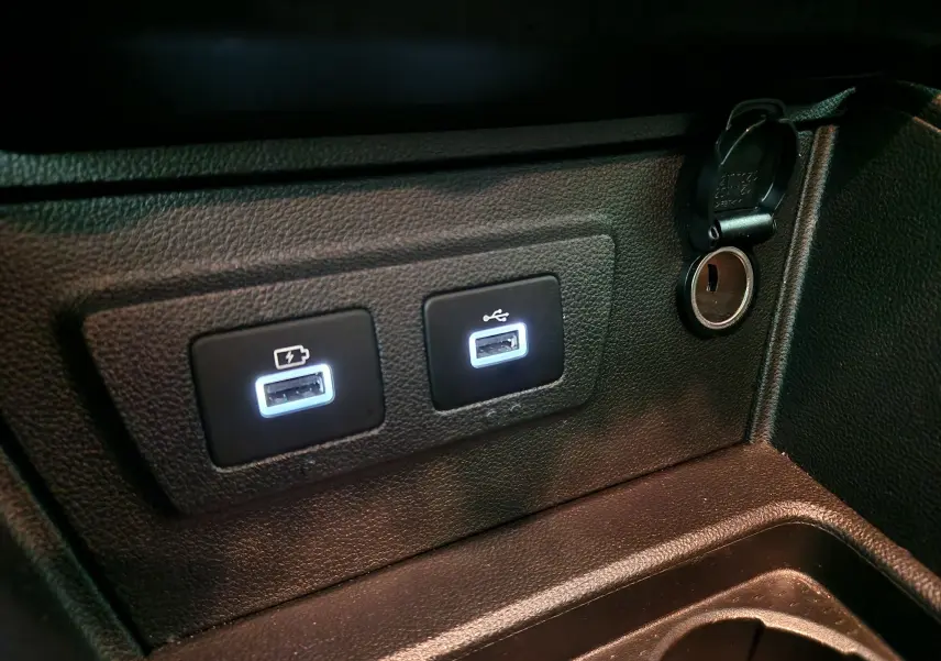 Prise USB double éclairée et prise 12V dans l'habitacle du Dacia Duster 4x4 blanc 2024, détail console centrale.