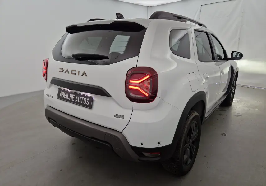 Vue arrière droite du Dacia Duster blanc 4x4 2024 avec feux LED distinctifs et barres de toit noires.