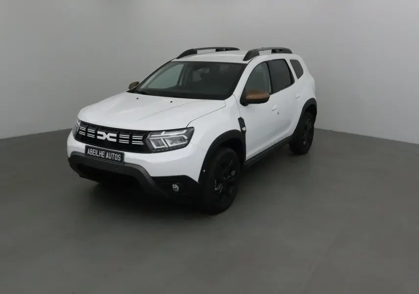 Dacia Duster 4x4 blanc en 3/4 avant droit avec coques de rétroviseurs bronze et jantes noires.