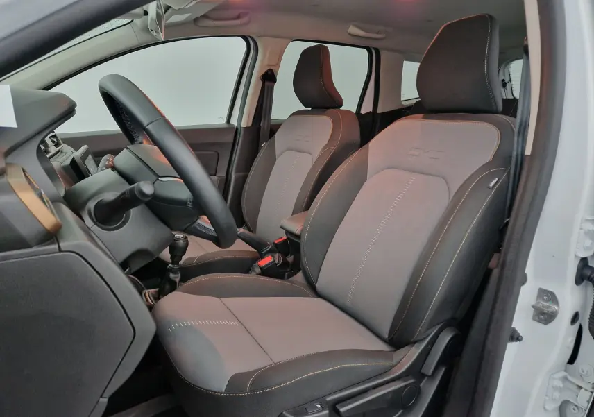 Intérieur du Dacia Duster 2024 blanc, vue côté gauche sur les sièges avant en tissu gris avec coutures contrastées.