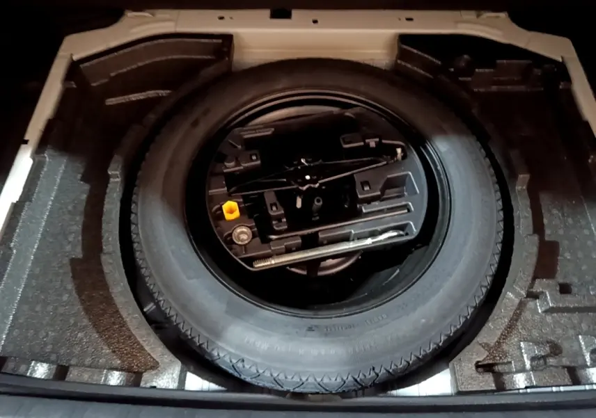 Vue plongeante sur la roue de secours et les outils de bord dans le coffre d'une Peugeot 308 blanche.