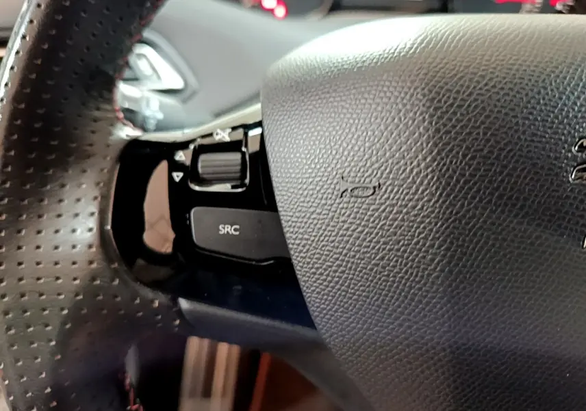 Gros plan sur le volant cuir perforé côté gauche du Peugeot 308 GT Line blanc avec commandes audio intégrées.