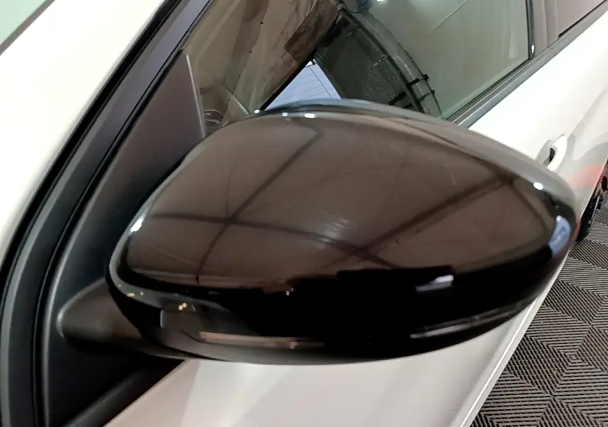 Gros plan sur le rétroviseur noir côté gauche d'une Peugeot 308 blanche, reflet du plafond visible.