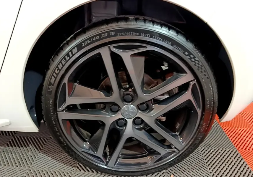 Gros plan sur la roue avant droite noire brillante d'une Peugeot 308 blanche Puretech 130 S&S GT Line 2019.