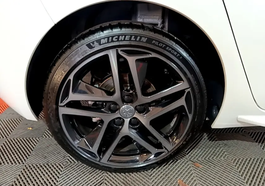 Gros plan sur la roue arrière droite noire brillante de la Peugeot 308 blanche, mettant en valeur la jante sport et le pneu Michelin.