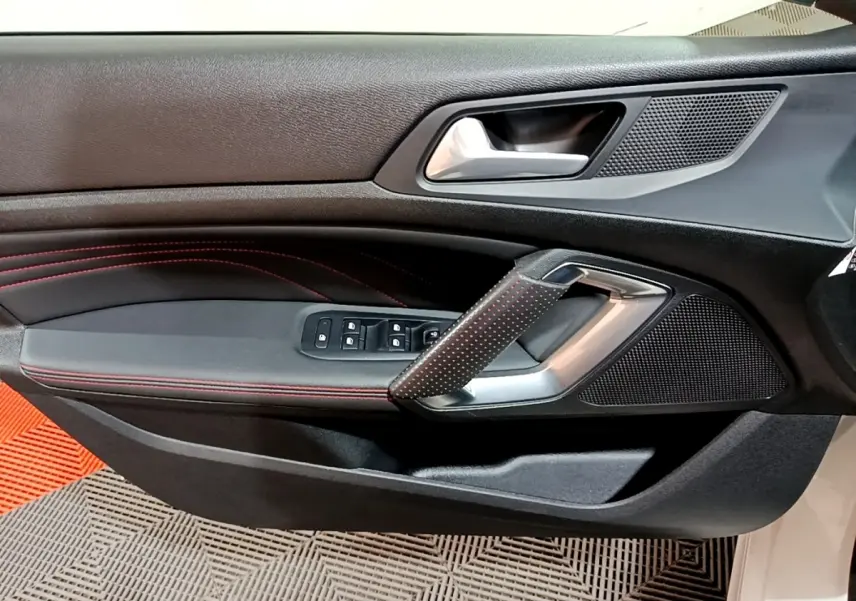 Vue rapprochée de la porte côté conducteur de la Peugeot 308 GT Line blanche, avec surpiqûres rouges et commandes électriques.