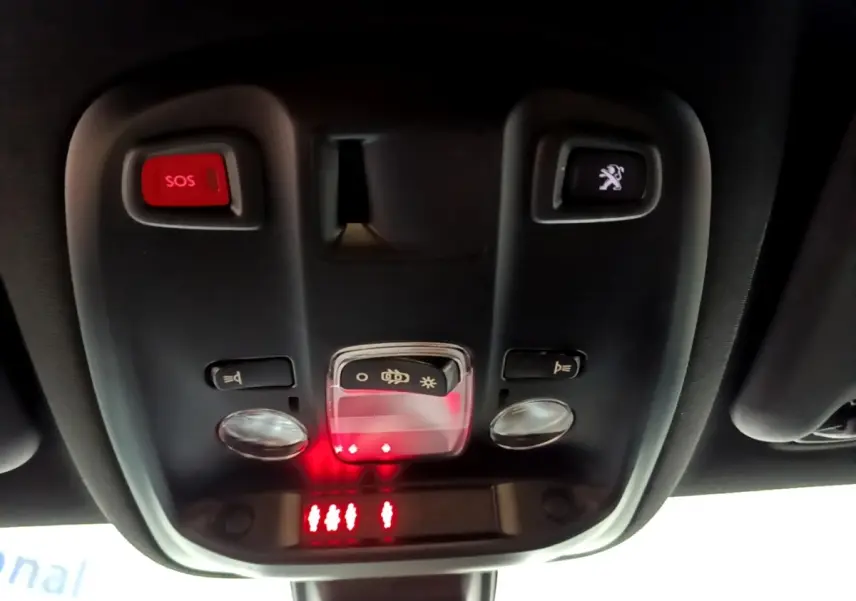 Vue en contre-plongée du plafonnier noir avec bouton SOS rouge et commande d'éclairage dans une Peugeot 308 blanche.