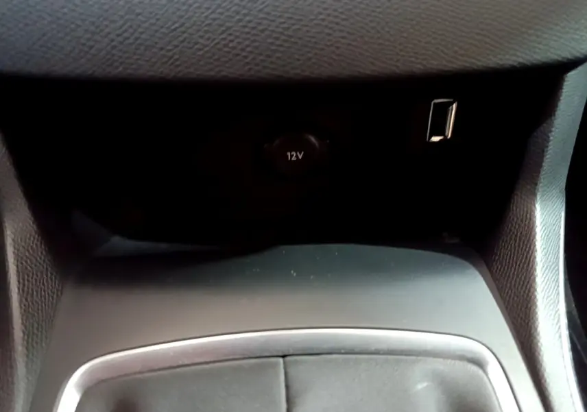 Prise 12V et port USB en gros plan dans l’espace de rangement central d’une Peugeot 308 blanche.