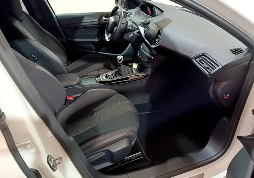 Intérieur côté conducteur de Peugeot 308 blanc, montrant sièges noirs avec surpiqûres rouges et tableau de bord moderne.