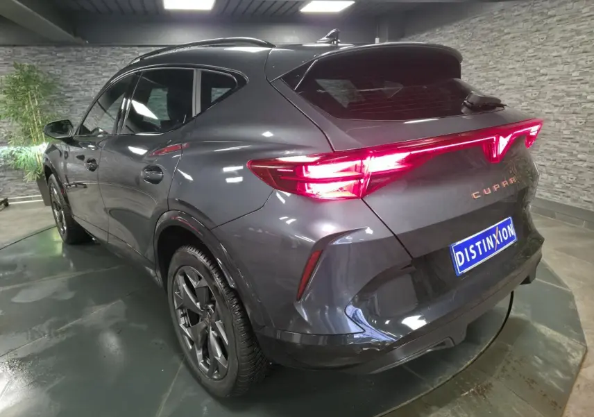 Vue 3/4 arrière droite du CUPRA Formentor gris métallisé avec feux arrière Tri-LED allumés et jantes alliage 18 pouces.