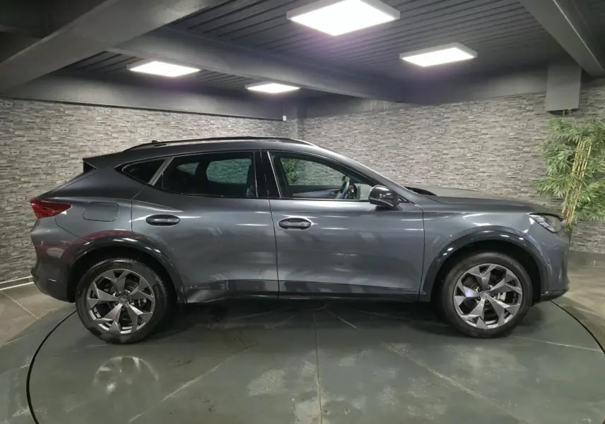 Vue de profil côté gauche du CUPRA Formentor gris métallisé avec jantes alliage 18'' et toit noir dans un garage.