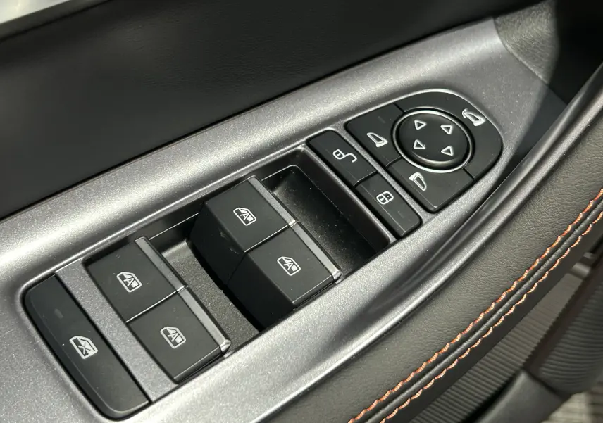Gros plan sur les commandes de lève-vitres et réglages des rétroviseurs côté conducteur, avec surpiqûres orange sur cuir noir.