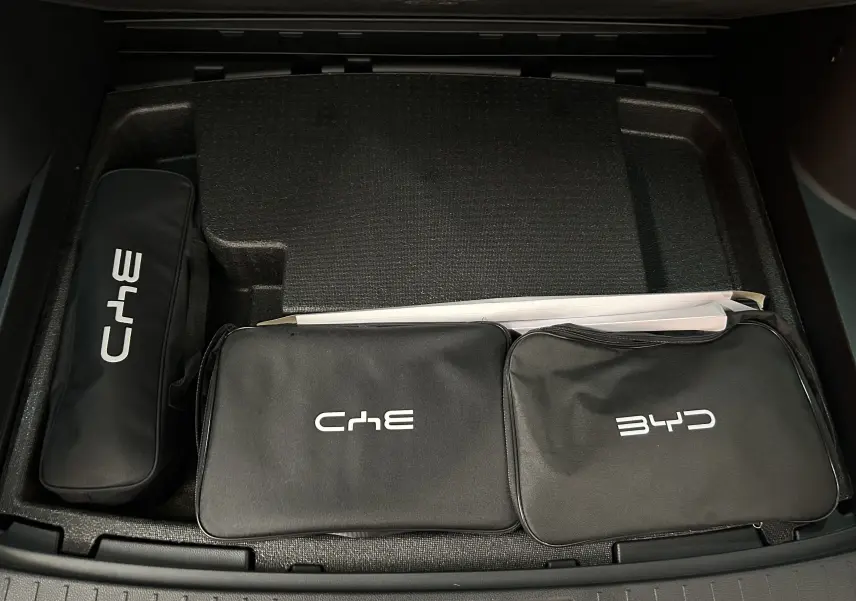 Vue plongeante sur le coffre avec trois trousses noires de marque BYD et ChE, sur fond intérieur noir.