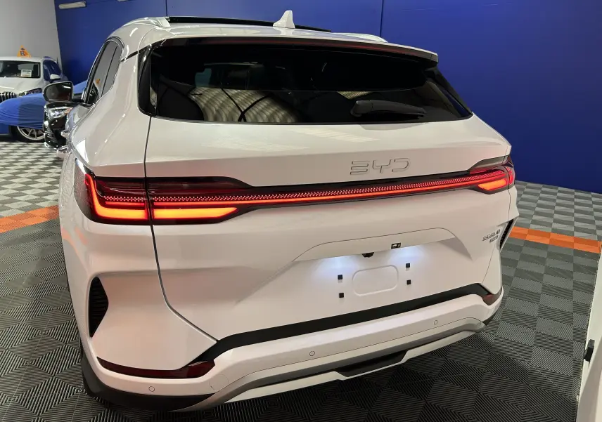 Vue 3/4 arrière d'un BYD SEAL U blanc nacré avec feux arrière LED allumés et hayon électrique en intérieur showroom.