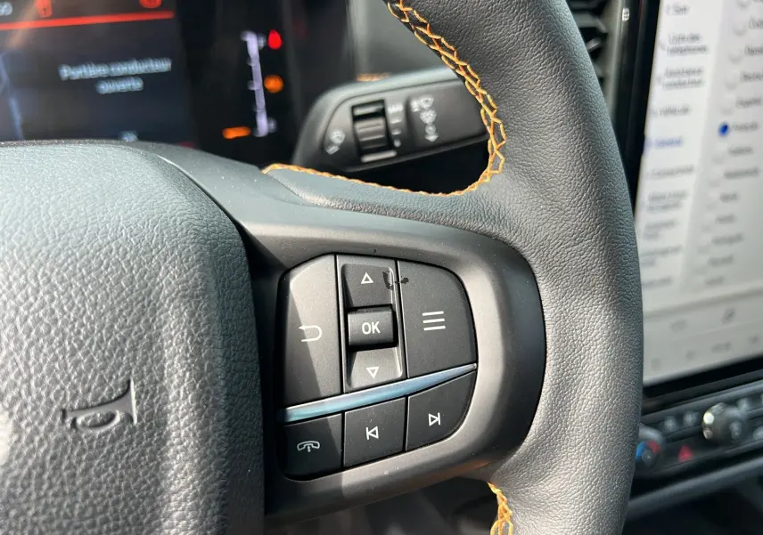 Gros plan sur le volant cuir noir avec surpiqûres orange du Ford Ranger Wildtrak 2026, boutons multifonctions visibles.