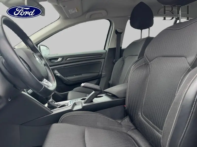 Vue intérieure côté conducteur montrant les sièges noirs, le volant cuir multifonction et la console centrale d'une Renault Mégane Break.