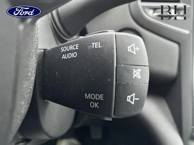 Gros plan sur la commande audio au volant noir, avec boutons volume et mode, intérieur d'une Renault Mégane Break gris platine.