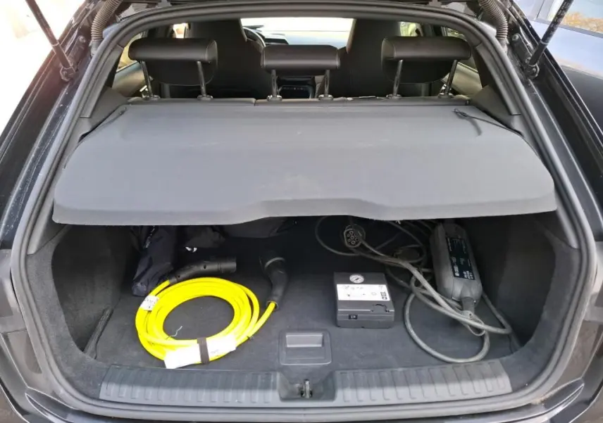 Coffre ouvert d’une Audi A3 Sportback noire, vue arrière, avec câble de recharge jaune et accessoires visibles.