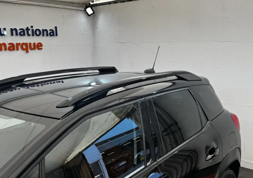 Vue 3/4 arrière gauche d’un Citroën C3 Aircross noir avec barres de toit et vitres teintées dans un garage.
