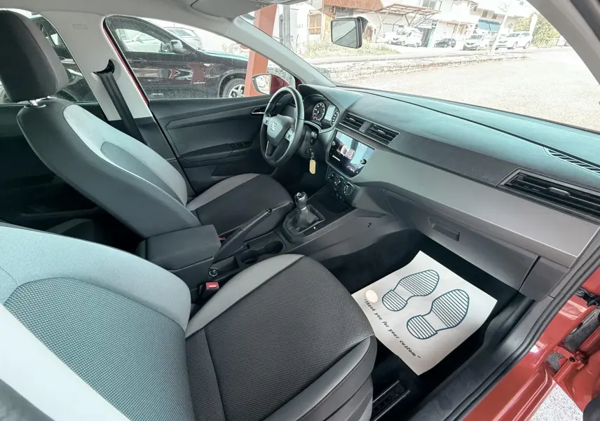 Vue intérieure côté passager d'une SEAT Ibiza rouge passion 2020, montrant sièges gris et tableau de bord moderne.