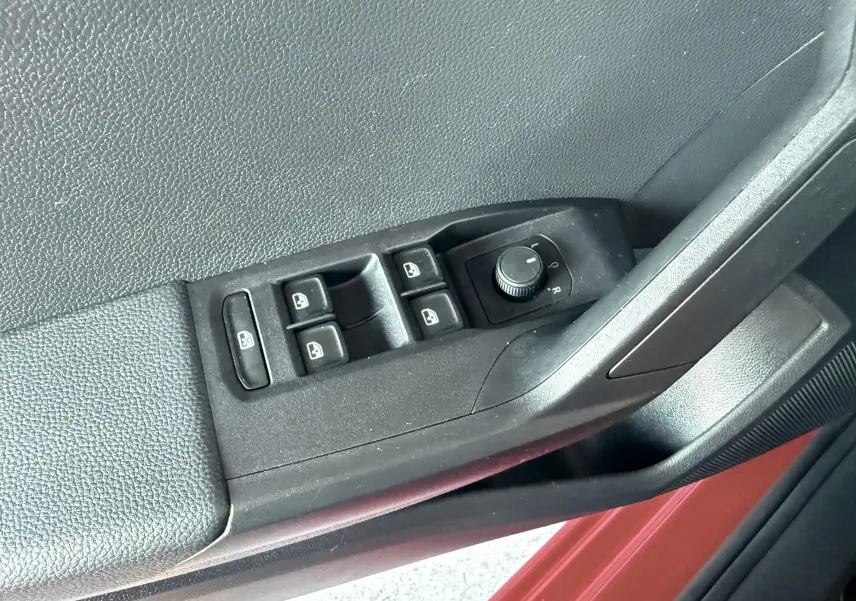 Gros plan sur les commandes électriques des vitres et rétroviseurs côté conducteur d'une SEAT Ibiza rouge passion.