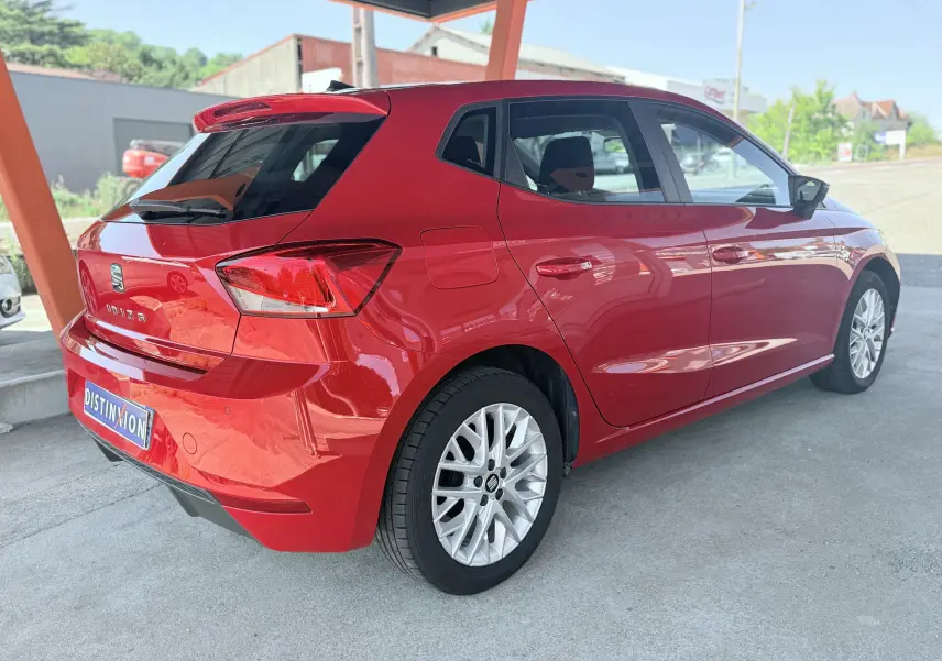 Vue 3/4 arrière droite d'une SEAT Ibiza rouge passion métallisé avec jantes alliage et cinq portes sous abri.