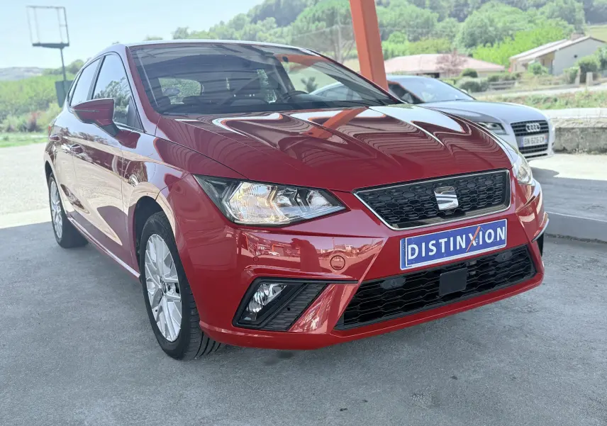 SEAT Ibiza rouge passion vue 3/4 avant droit, avec calandre noire et phares allumés sous abri.