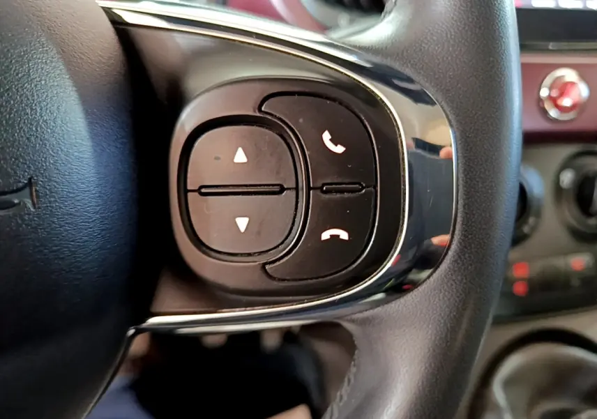 Gros plan sur les commandes noires du volant cuir à droite dans l'habitacle rouge d'une FIAT 500 1.0 70ch BSG Star 2021.