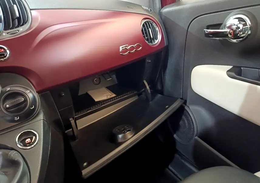 Intérieur côté passager d'une Fiat 500 rouge 2021 avec boîte à gants ouverte et tableau de bord assorti.