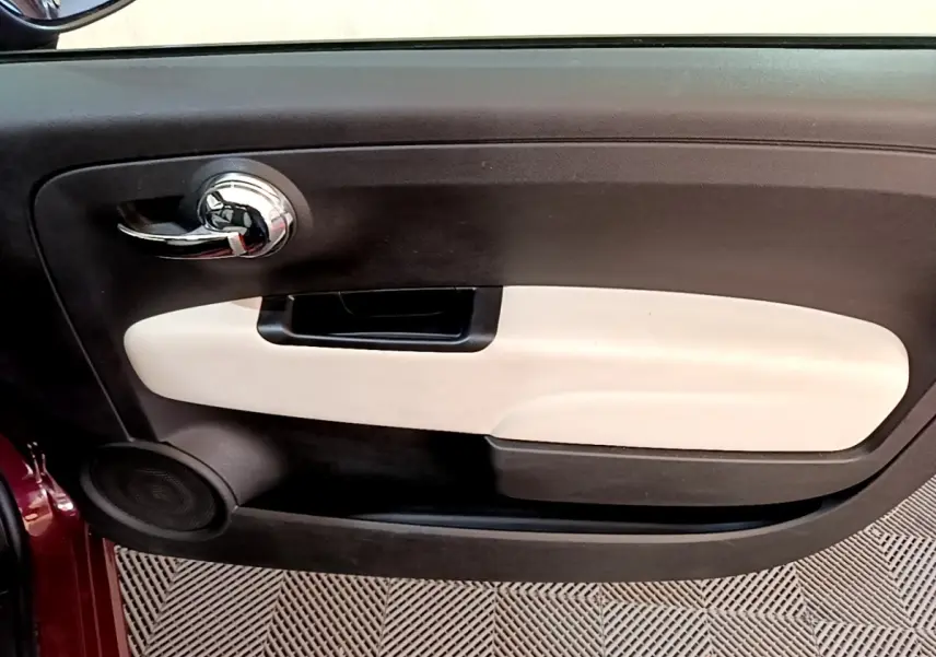 Intérieur de la porte côté gauche de la Fiat 500 rouge, avec poignée chromée et panneau beige contrastant.