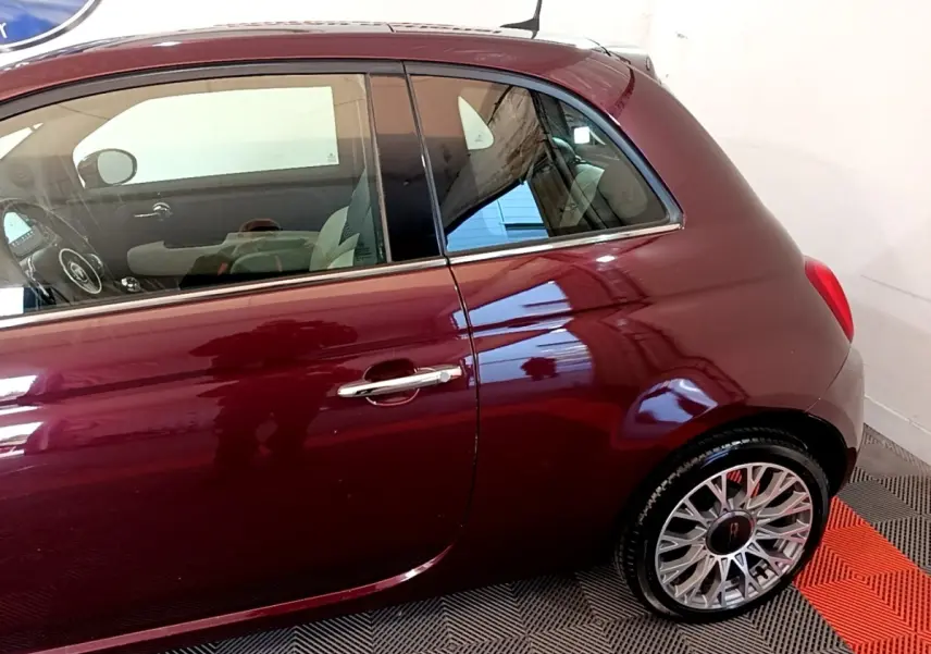 Profil côté gauche d'une FIAT 500 rouge bordeaux 2021 avec jantes alliage et poignée de porte chromée.