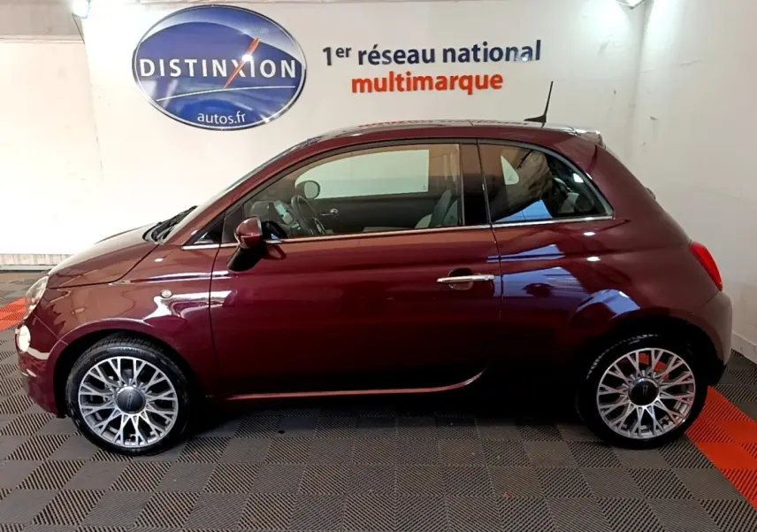Profil côté gauche d'une FIAT 500 rouge bordeaux 2021, avec jantes alliage et toit compact en intérieur showroom.