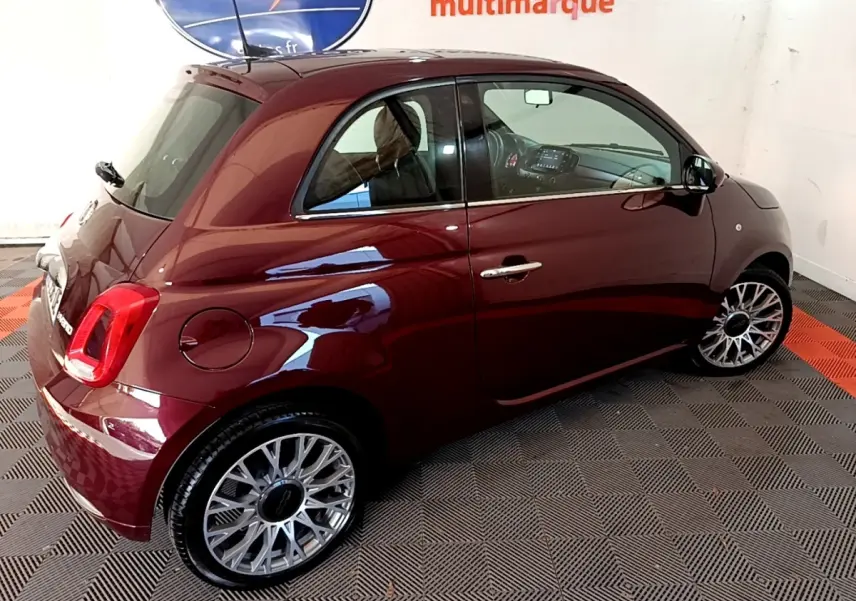 Vue 3/4 arrière droite d'une FIAT 500 rouge brillante avec jantes alliage et intérieur visible par la vitre.