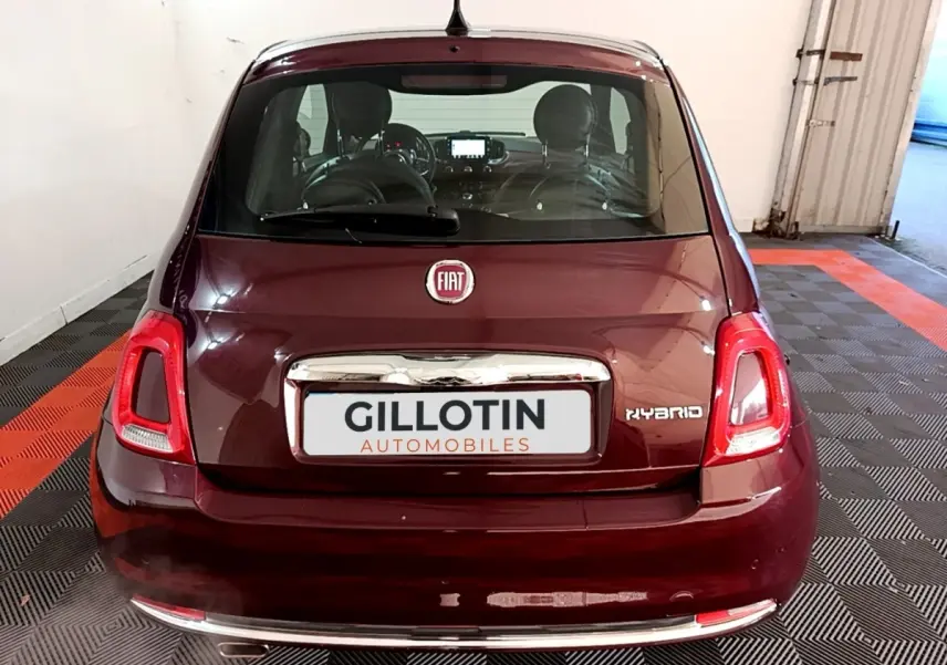 Vue arrière d'une FIAT 500 rouge hybride avec logo FIAT et badge Hybrid visible sur un sol damier noir et rouge.