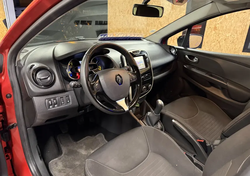Intérieur côté conducteur d'une Renault Clio Estate IV rouge, montrant le tableau de bord et la boîte manuelle.