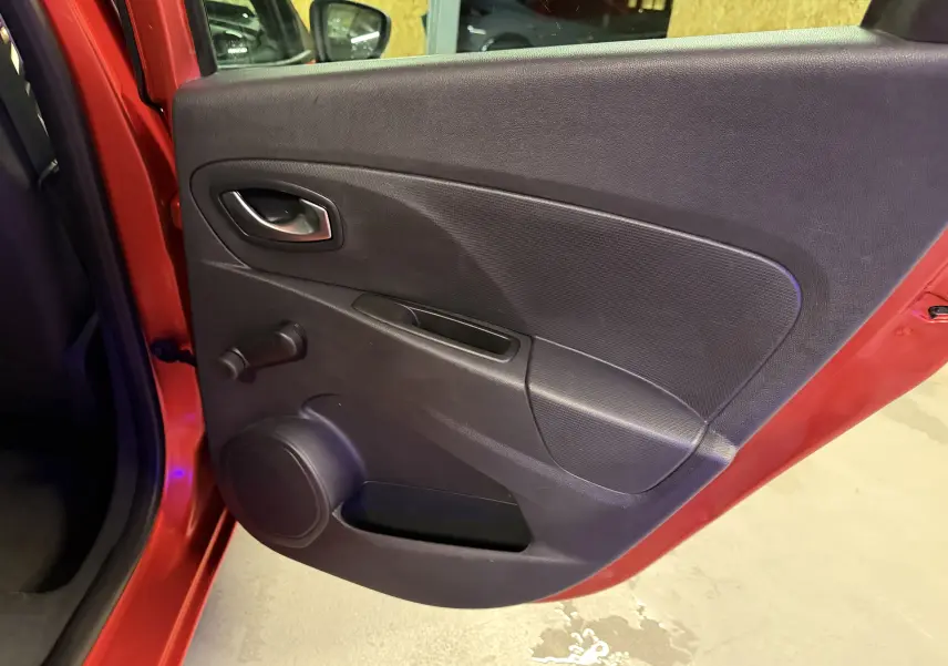 Porte arrière gauche ouverte d'une Renault Clio Estate IV rouge, montrant le panneau intérieur noir avec poignée et manivelle de vitre.