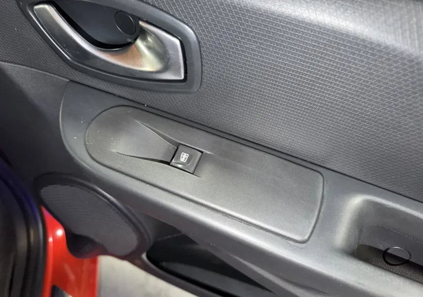 Détail de la poignée intérieure côté gauche d'une Renault Clio Estate IV rouge avec commande de lève-vitre électrique.