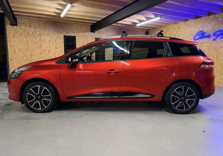 Profil droit d'une Renault Clio Estate IV rouge de 2015 avec barres de toit et jantes alliage noires.
