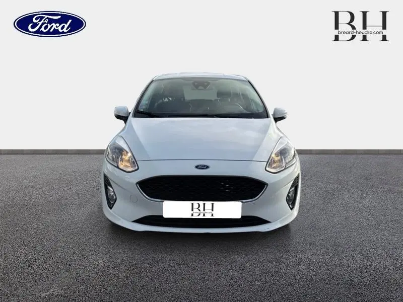 Vue de face d'une Ford Fiesta blanche Glacier 2020 avec calandre noire et phares allumés sur fond neutre.